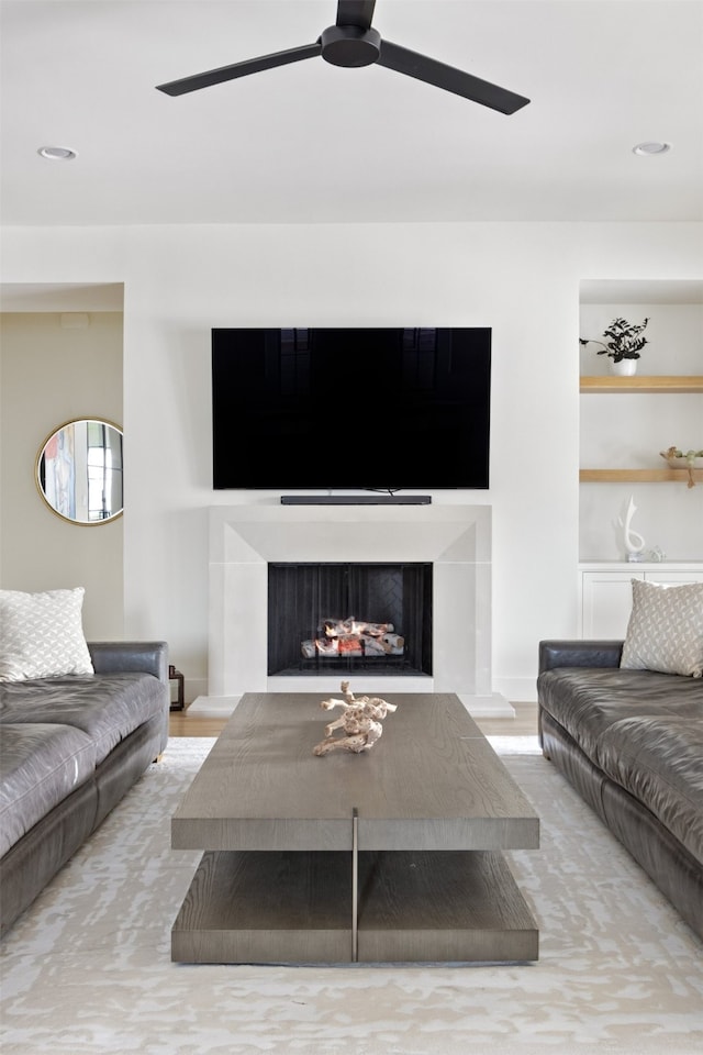 living room with a fireplace with raised hearth and a ceiling fan