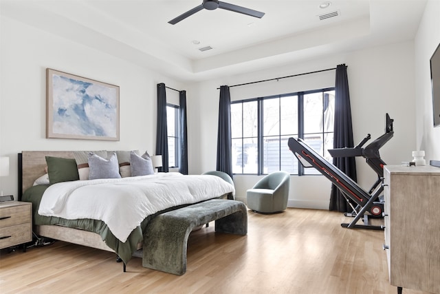 bedroom with a raised ceiling, light wood-style floors, and visible vents