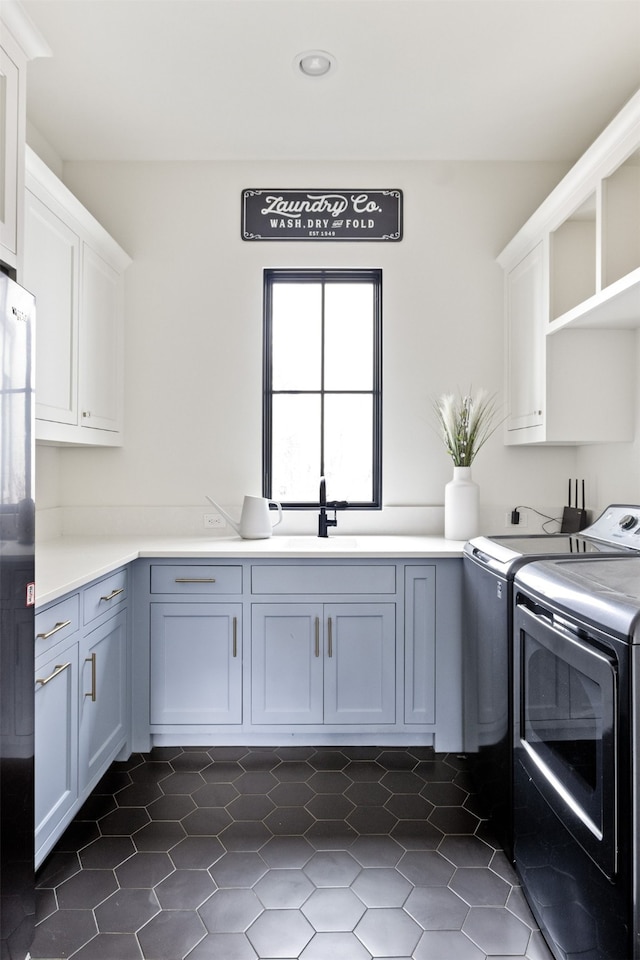 clothes washing area with a sink, cabinet space, dark tile patterned flooring, and independent washer and dryer