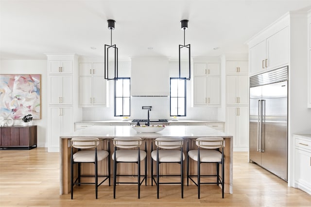 kitchen with stainless steel built in refrigerator, white cabinets, light wood-type flooring, and an island with sink