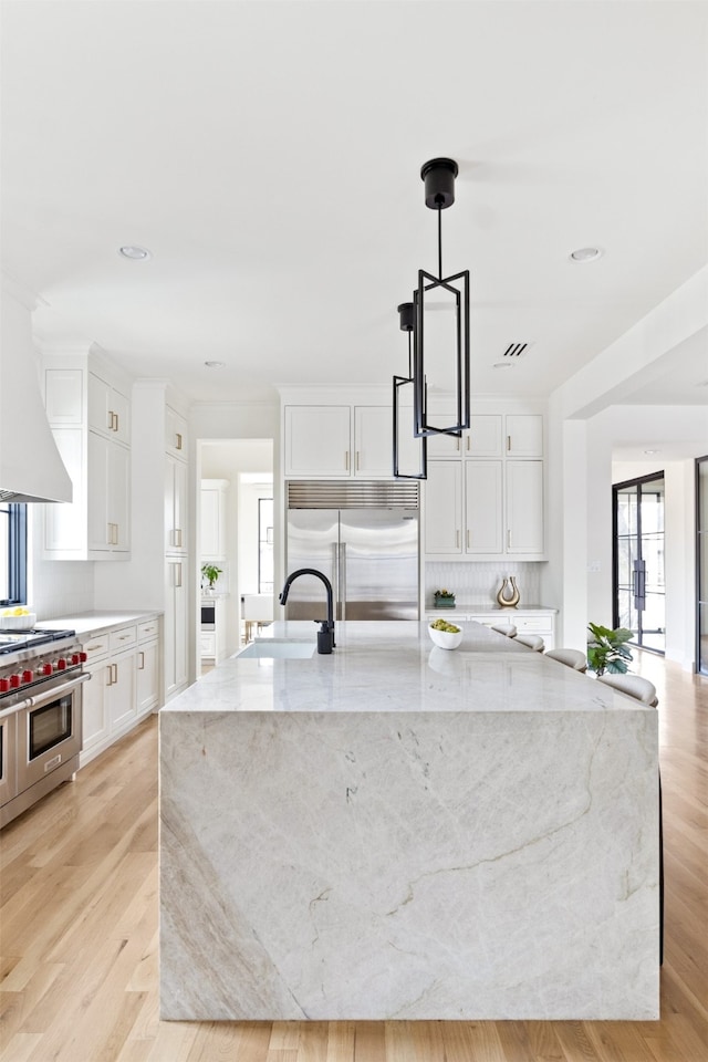 kitchen featuring a spacious island, light wood-type flooring, premium appliances, white cabinets, and a sink