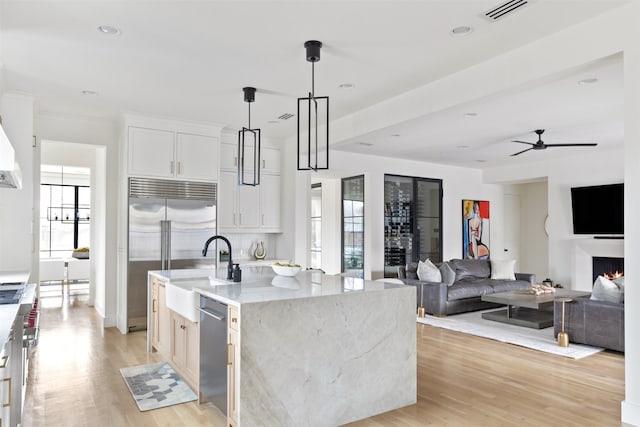 kitchen featuring light stone counters, stainless steel appliances, light wood-style floors, and a center island with sink