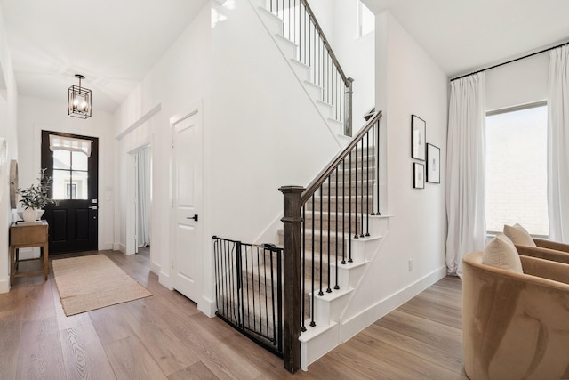 foyer entrance with a notable chandelier, stairway, baseboards, and light wood-style floors