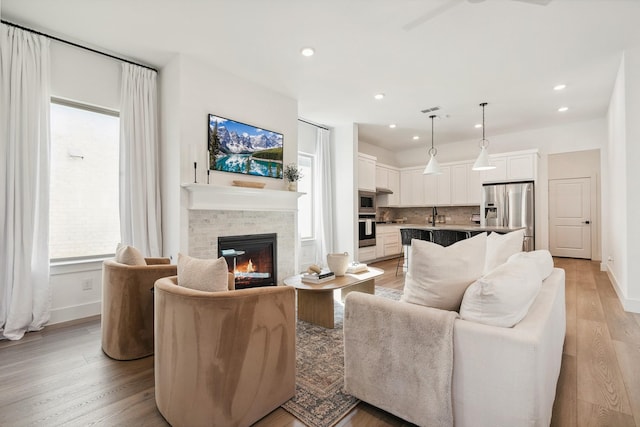 living room with recessed lighting, a glass covered fireplace, light wood-style flooring, and baseboards