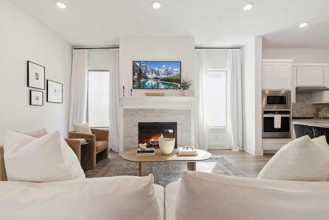 living room with a tiled fireplace, recessed lighting, and light wood finished floors