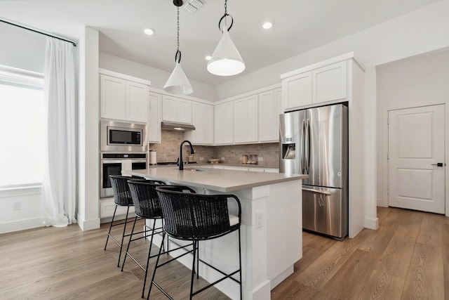 kitchen featuring light wood-type flooring, light countertops, appliances with stainless steel finishes, a kitchen breakfast bar, and tasteful backsplash