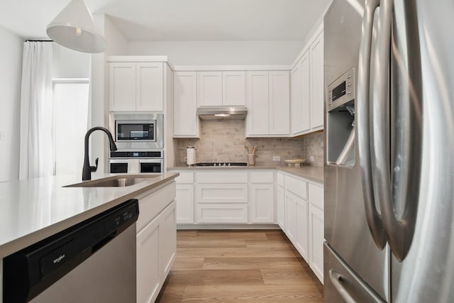 kitchen with light wood finished floors, under cabinet range hood, light countertops, stainless steel appliances, and a sink