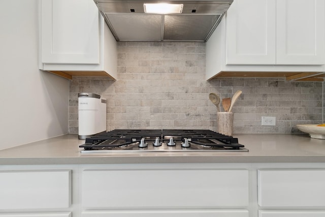 kitchen featuring tasteful backsplash, range hood, white cabinetry, stainless steel gas stovetop, and light countertops