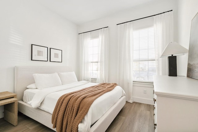 bedroom with multiple windows, wood finished floors, and baseboards