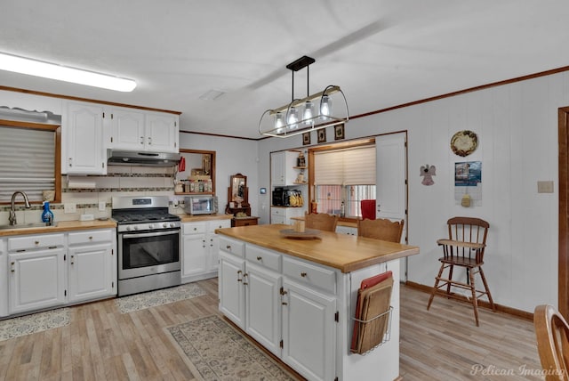 kitchen with stainless steel gas range oven, under cabinet range hood, ornamental molding, light wood-style floors, and white cabinets