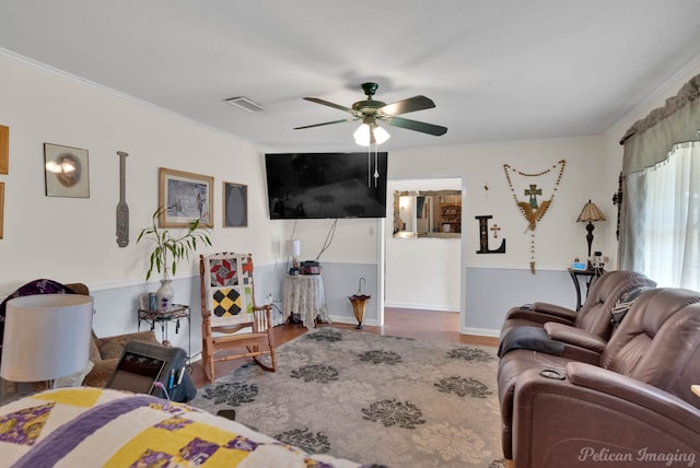 living area with visible vents, wood finished floors, ornamental molding, and a ceiling fan