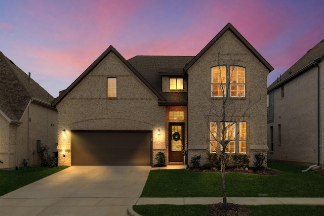 french provincial home with brick siding, a lawn, an attached garage, and concrete driveway