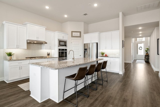 kitchen with visible vents, a kitchen island with sink, under cabinet range hood, appliances with stainless steel finishes, and dark wood-style flooring