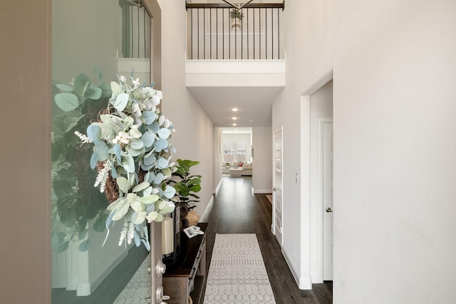 corridor featuring dark wood-type flooring, a high ceiling, and baseboards