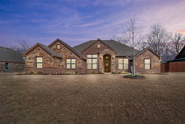 french country home featuring stone siding, brick siding, a front yard, and fence