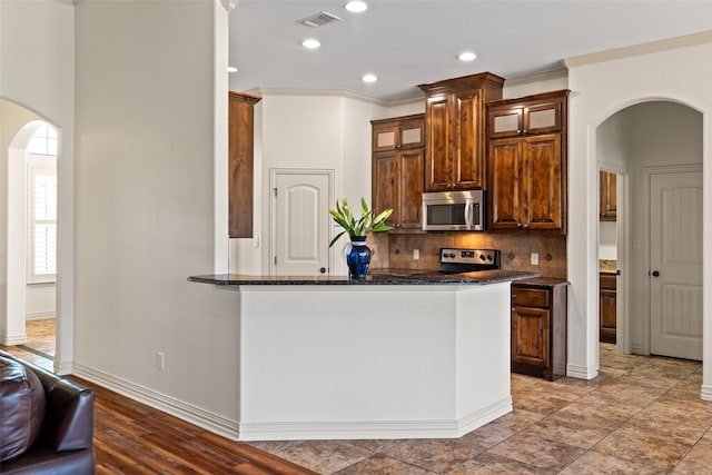 kitchen with tasteful backsplash, glass insert cabinets, arched walkways, and appliances with stainless steel finishes