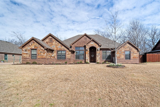 view of front of property featuring brick siding, a front lawn, fence, roof with shingles, and stone siding