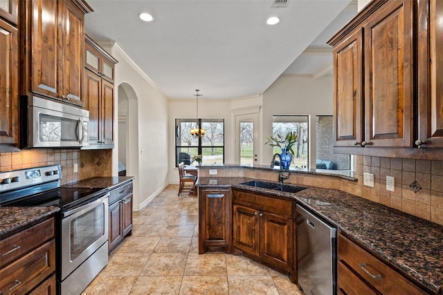 kitchen with a notable chandelier, a sink, dark stone counters, appliances with stainless steel finishes, and a peninsula