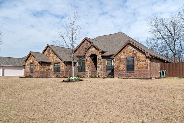 view of front facade featuring a front lawn, stone siding, fence, a garage, and brick siding