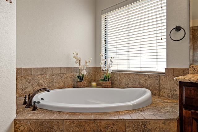 bathroom with a garden tub, vanity, and a textured wall