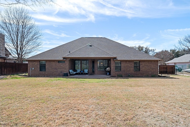 rear view of house with a lawn, fence, roof with shingles, brick siding, and a patio area