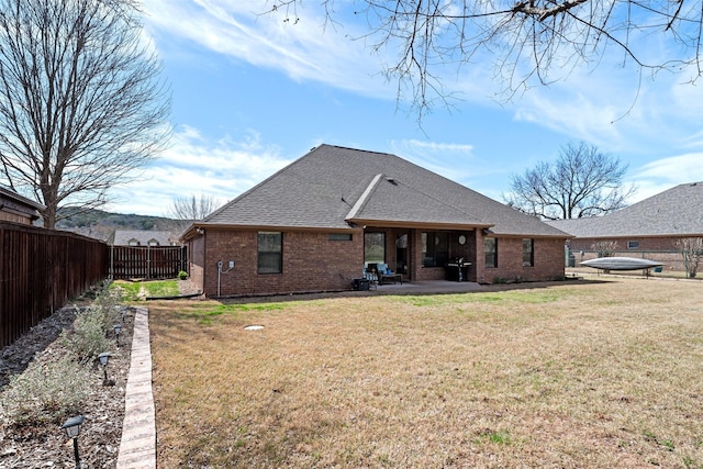 rear view of house featuring roof with shingles, a yard, a fenced backyard, a patio area, and brick siding