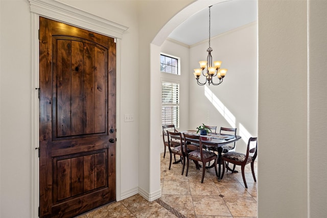 foyer entrance with arched walkways, a notable chandelier, baseboards, and ornamental molding