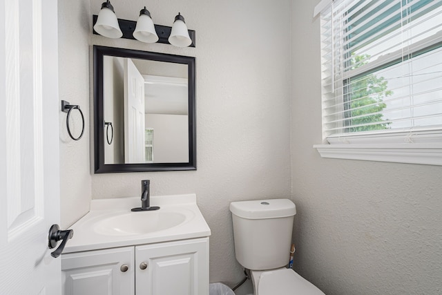 half bathroom featuring vanity, toilet, and a textured wall