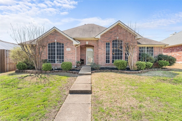 ranch-style home featuring brick siding, a shingled roof, a front yard, and fence