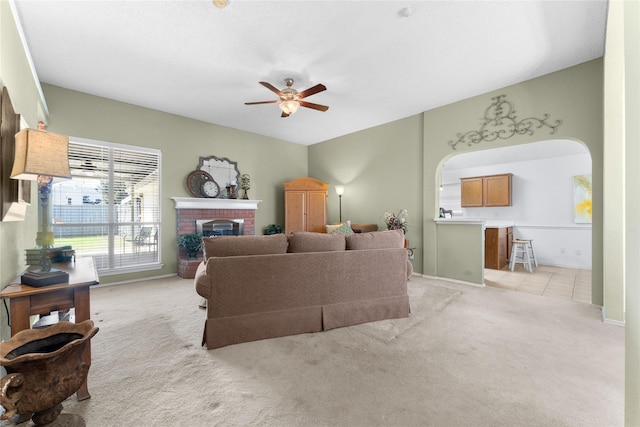 living area with arched walkways, light colored carpet, a fireplace, and a ceiling fan