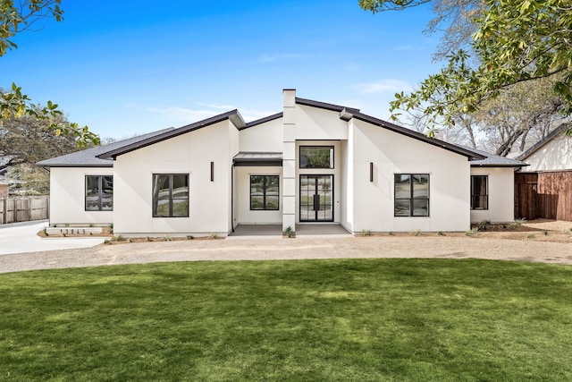 back of house featuring stucco siding, a lawn, and fence