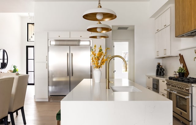 kitchen with visible vents, light wood finished floors, a sink, premium appliances, and light countertops