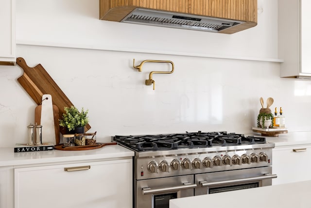 kitchen featuring white cabinetry, light countertops, range with two ovens, and ventilation hood