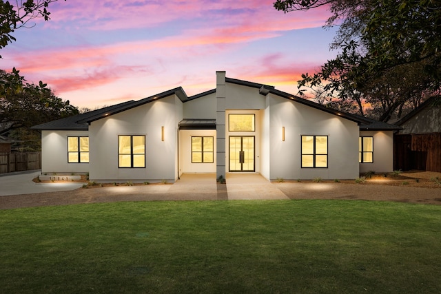 back of property at dusk featuring stucco siding, a patio, a lawn, and fence