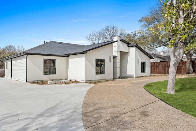 view of front of property featuring a front yard, fence, roof with shingles, and curved driveway