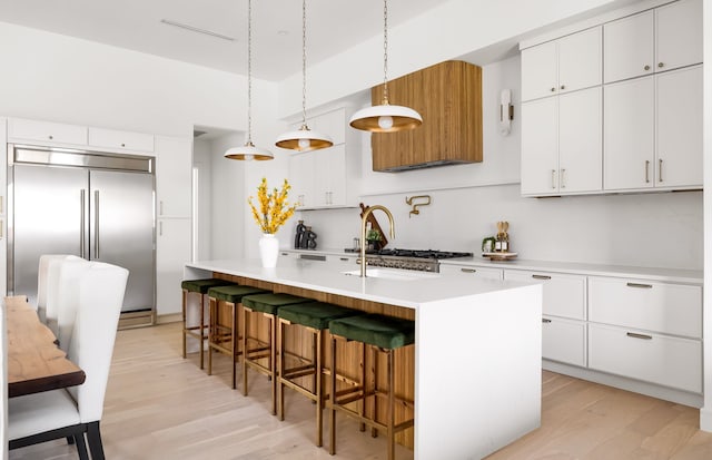 kitchen featuring a center island with sink, light wood-style flooring, light countertops, white cabinets, and built in refrigerator