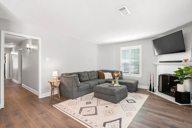 living area featuring dark wood-type flooring, a brick fireplace, baseboards, and visible vents