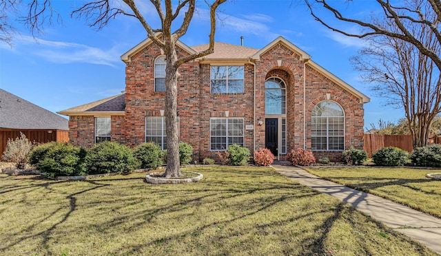 traditional-style home featuring brick siding, roof with shingles, a front lawn, and fence