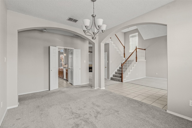 carpeted empty room featuring visible vents, an inviting chandelier, tile patterned flooring, stairs, and a textured ceiling