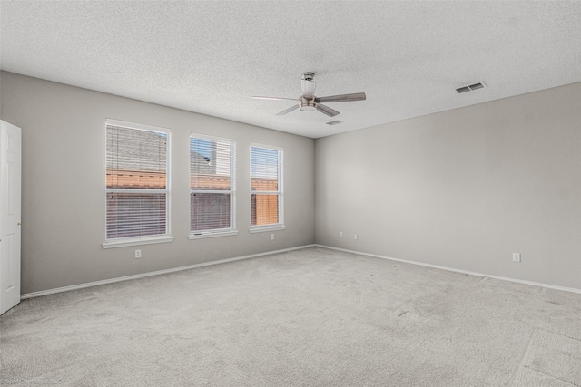 carpeted spare room featuring a textured ceiling, baseboards, visible vents, and ceiling fan