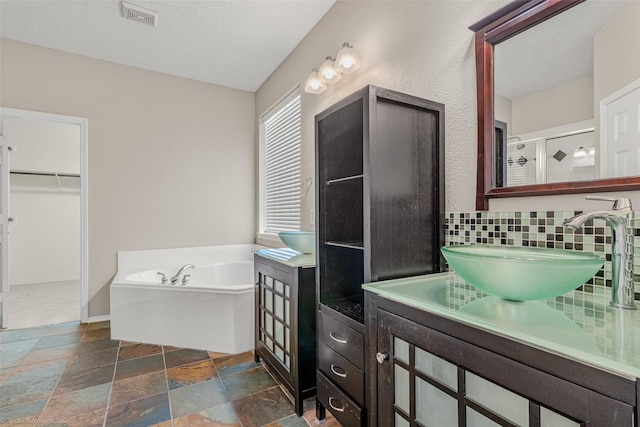 full bathroom featuring visible vents, backsplash, a bath, stone finish floor, and a textured ceiling