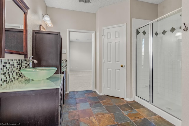 bathroom featuring backsplash, a shower stall, baseboards, stone finish floor, and a textured ceiling