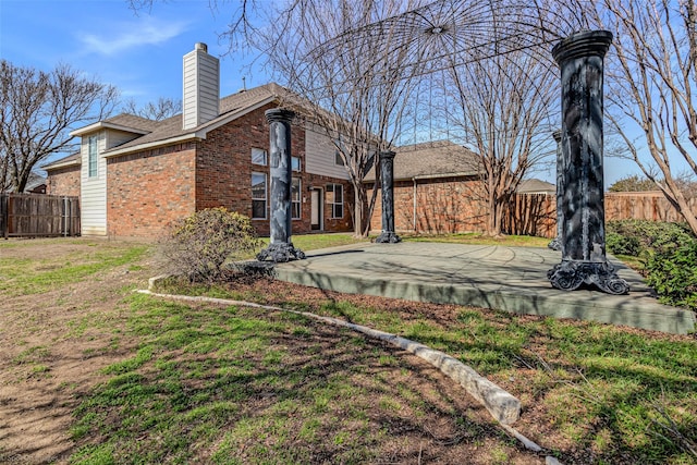 rear view of property featuring brick siding, a chimney, a yard, and fence