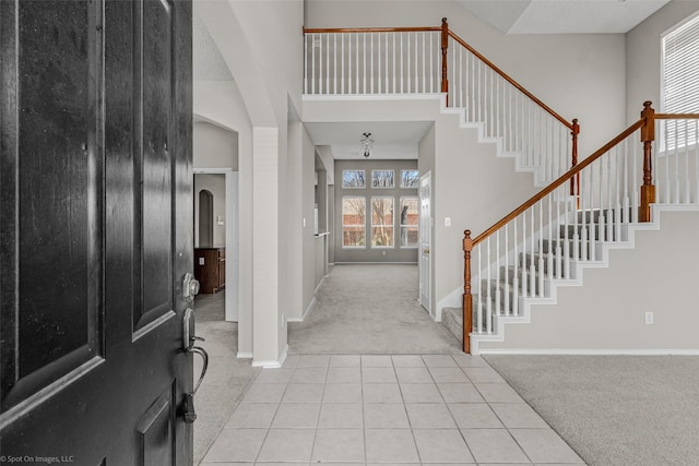 entryway featuring light tile patterned floors, baseboards, arched walkways, a towering ceiling, and light colored carpet