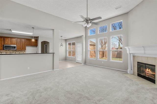 unfurnished living room with visible vents, baseboards, ceiling fan, light colored carpet, and a fireplace