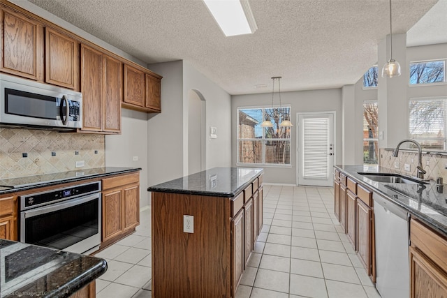 kitchen with light tile patterned floors, dark stone countertops, brown cabinetry, stainless steel appliances, and a sink