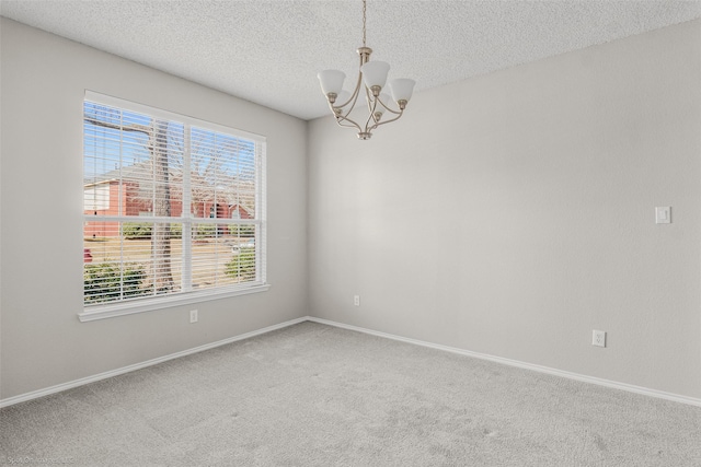 unfurnished room with carpet flooring, a textured ceiling, baseboards, and an inviting chandelier