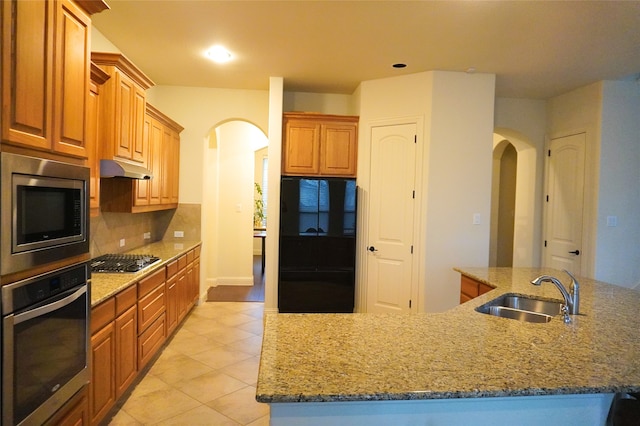 kitchen featuring arched walkways, a sink, under cabinet range hood, appliances with stainless steel finishes, and tasteful backsplash