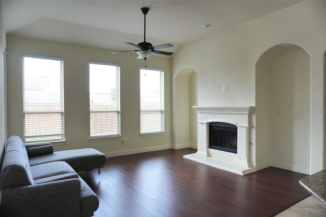 living area featuring lofted ceiling, a fireplace with raised hearth, wood finished floors, and ceiling fan