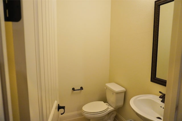 half bathroom with toilet, baseboards, and a sink